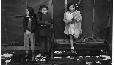 a black and white photo of 3 girls standing in front of a barrack